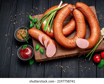 Dry Appetizing Smoked Pork Sausage On A Dark Background With Different Spices And Vegetables. Photo For The Menu