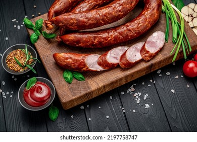 Dry Appetizing Smoked Pork Sausage On A Dark Background With Different Spices And Vegetables. Photo For The Menu