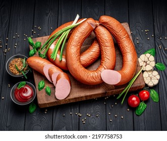 Dry Appetizing Smoked Pork Sausage On A Dark Background With Different Spices And Vegetables. Photo For The Menu