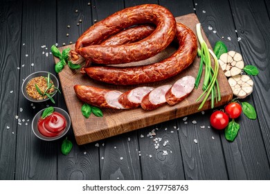 Dry Appetizing Smoked Pork Sausage On A Dark Background With Different Spices And Vegetables. Photo For The Menu