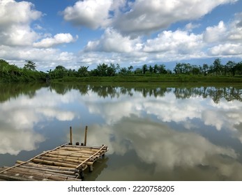 Dry Bamboo Bridge By The Lake With Calm Water Reflection Of Green Tree Landscape With Clear Sky View. Concept Of Silence