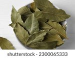 Dry bay leaves in bowl on white wooden table, closeup