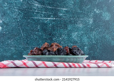 Dry black plums and dates in a blue platter, Ajwa dates. Dried date fruit of the ajwa type, Ajwa dates isolated in a plate on a white marble table, Madina Saudi Arabian dates, the most luxurious.