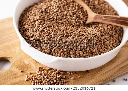 dry buckwheat groats in a white bowl on a wooden board with a wooden spoon, on a white background, top view, close-up