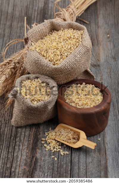 Dry bulgur\
wheat grains on wooden background. Vegetarian cuisine - dry bulgur\
for cooking. Wheat grains that have been steamed, dried and\
crushed; a staple of Middle Eastern\
cooking