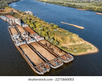 Dry cargo barges stand empty moored to green river island