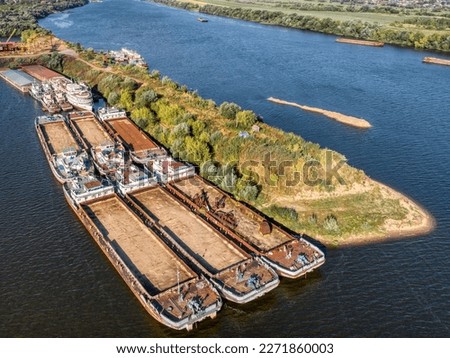 Dry cargo barges stand empty moored to green river island