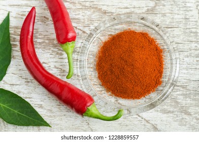 Dry chili pepper powder and fresh red chili pepper pods on the old shabby wooden background. Top view.

