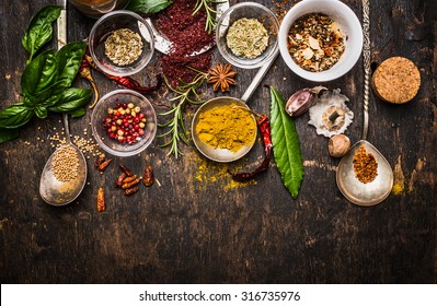 Dry colorful  spices in spoons and bowls with fresh seasoning on dark rustic wooden background, top view, border