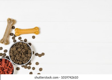 Dry Dog Pet Food In Bowl On White Wooden Background Top View. Pet Feeding Concept Backgrounds With Copy Space. Photograph Taken From Above.