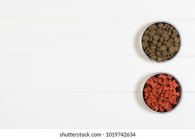 Dry Dog Pet Food In Bowl On White Wooden Background Top View. Pet Feeding Concept Backgrounds With Copy Space. Photograph Taken From Above.