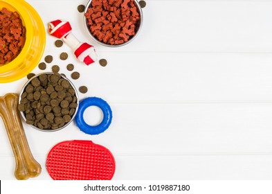 Dry Dog Pet Food In Bowl And Accessories On White Wooden Background Top View. Pet Feeding And Care Concept Backgrounds With Copy Space. Photograph Taken From Above.