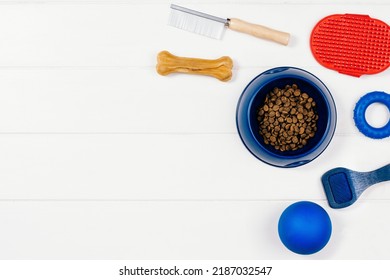 Dry Dog Pet Food In Bowl And Accessories On White Wooden Background Top View. Pet Feeding And Care Concept Background With Copy Space. Photograph Taken From Above.