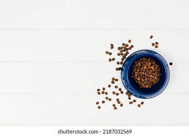 Dry Dog Pet Food In Bowl And Accessories On White Wooden Background Top View. Pet Feeding And Care Concept Background With Copy Space. Photograph Taken From Above.