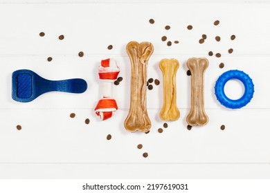 Dry Dog Pet Food In Bowl And Accessories On White Wooden Background Top View. Pet Feeding And Care Concept Background With Copy Space. Photograph Taken From Above.