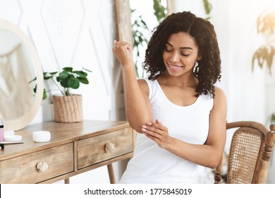 Dry Elbows Treatment. Smiling Black Woman Applying Moisturising Cream At Home, Healing Cracked Skin