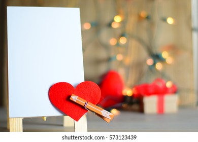 Dry Erase Board With Small Arrow Going Through Felt Heart, With Blurred Lights And Present In The Background.