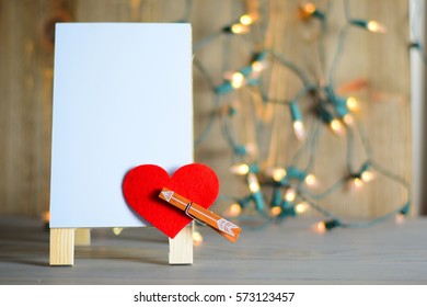 Dry Erase Board With Small Arrow Going Through Felt Heart, With Blurred Lights In The Background.