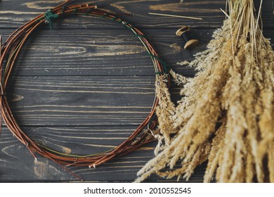 Dry grass and twigs in circle on rustic wooden dark background. Making stylish boho autumn wreath with wildflowers and herbs. Space for text. Holiday workshop