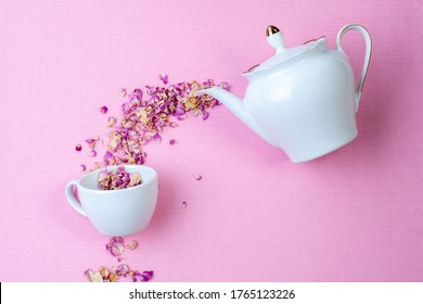 Dry Herbal Tea Is A Tea Rose Poured From A White Porcelain Teapot Into A Cup On A Pink Surface. View From Above. Tea Party Concept.