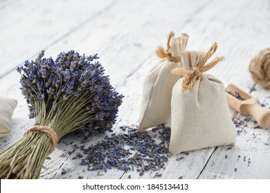 Dry lavender flower bouquets and aromatic sachets on white wooden table.