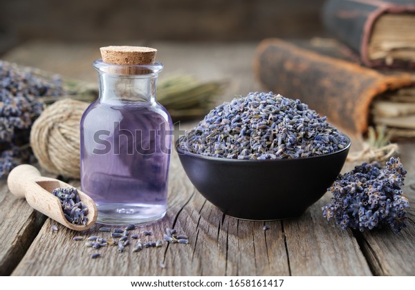 Dry lavender flowers in bowl and bottle of essential\
lavender oil or infused water. Old books and lavender flowers bunch\
on background. 