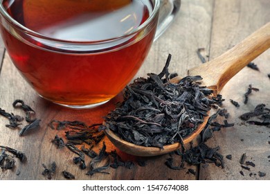 Dry Leaves Of Black Tea In A Wooden Spoon. A Cup Of Freshly Brewed Tea.