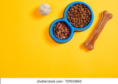 Dry Pet Food In Bowl With A Ball And Dog Bone On Yellow Background Top View