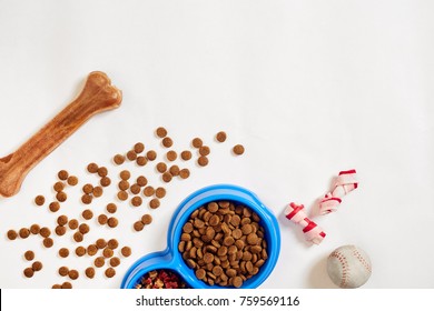 Dry Pet Food In Bowl With A Ball And Dog Bone On White Background Top View