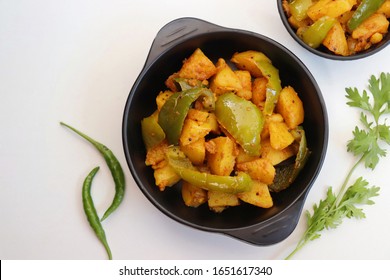 Dry Potatoes And Capsicum Curry Or Aloo Shimla Mirchi Ki Sabji Or Simla Mirch Masala Served In Black Bowl With Chilies And Coriander Over White Background With Copy Space.