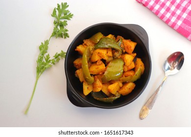 Dry Potatoes And Capsicum Curry Or Aloo Shimla Mirchi Ki Sabji Or Simla Mirch Masala Served In Black Bowl With Chilies And Coriander Over White Background With Copy Space.