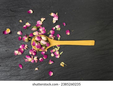 Dry Rose Buds, Roses Petals for Pink Flower Tea, Dried Persian Rosebuds, Rose Buds Textured Flowers in Wooden Spoon on Black Stone Plate Background