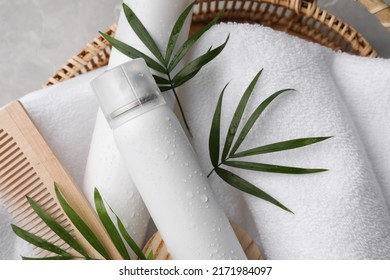 Dry shampoo sprays, towel and wooden comb with green leaves in wicker basket on table, top view - Shutterstock ID 2171984097