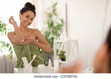 Dry Skin Treatment. Cheerful Millennial Woman In Towel Applying Moisturising Soothing Cream At Elbow Zone In Front Of Mirror At Home, Copy Space. Millennial Female Pampering Herself At Bathroom