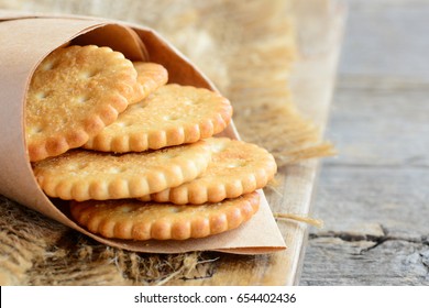 Dry thin crackers in a wrapping paper and on a sackcloth. Old wooden background. Tasty crispy crackers cookies idea for children and adults. Closeup