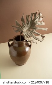 A Dry Tropical Plant Leaf, Split Leaf Philodendron, In An Old Clay Jar On A Light Brown And Beige Background. Creative Still Life Colorful Design. 