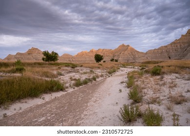 Dry Wash Runs Through Grassy Fields below Badlands Formations - Powered by Shutterstock