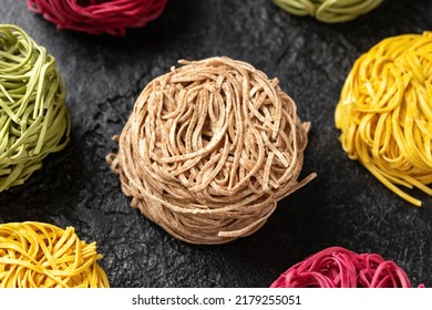Dry whole wheat, beetroot, spinach and egg noodles on rustic dark background