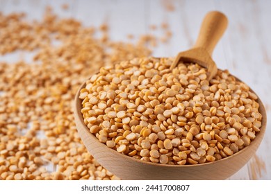 Dry yellow peas are scattered out of the wooden bowl on a light table, selective focus.