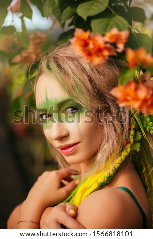 Dryad stands among the trees. Portrait of a beautiful girl with makeup on her face. Among the orange flowers. Forest Nymph
