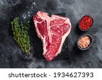 Dry-aged Raw T-bone or porterhouse beef meat Steak with herbs and salt. Black background. Top view.