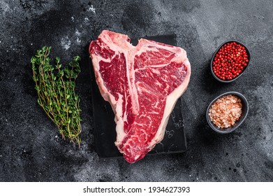 Dry-aged Raw T-bone or porterhouse beef meat Steak with herbs and salt. Black background. Top view. - Shutterstock ID 1934627393