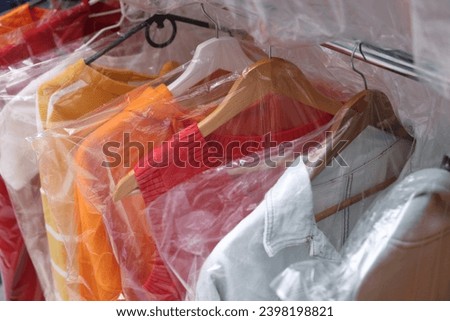 Dry-cleaning service. Hangers with different clothes in plastic bags on rack, closeup