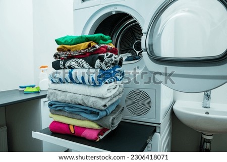 Dryer machine in a Landry room at home drying clothes. Big stack of clean, dry and folded clothes. Household chores concept 
