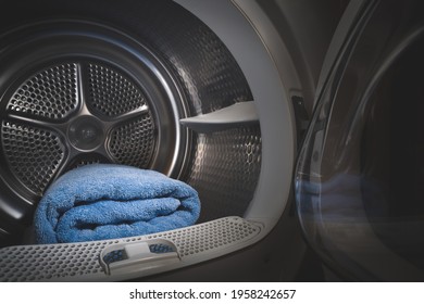 Dryer with open door in a dark room. Blue towels are stacked inside the drum.