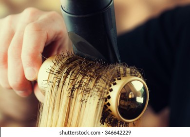 Drying blond hair with hair dryer and round brush. 