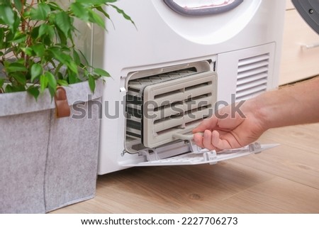 Drying machine with a full filter of lint, hair, dust, wool after the drying cycle of towels, bed linen. White drying machine. A man takes out a dirty radiator dryer. tumble dryer