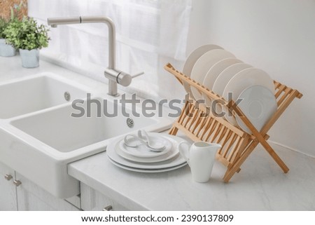 Drying rack with clean dishes on light marble countertop near sink in kitchen