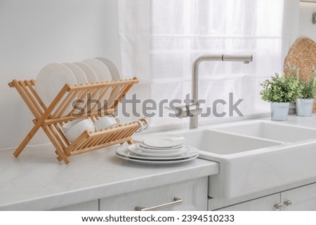 Drying rack with clean dishes on light marble countertop near sink in kitchen