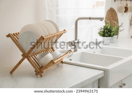 Drying rack with clean dishes on light marble countertop near sink in kitchen